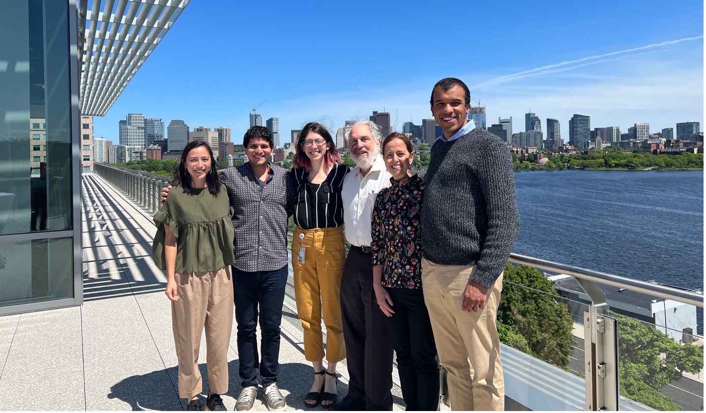 Group of six people standing on a roof deck outside, overlooking the Charles River and Boston