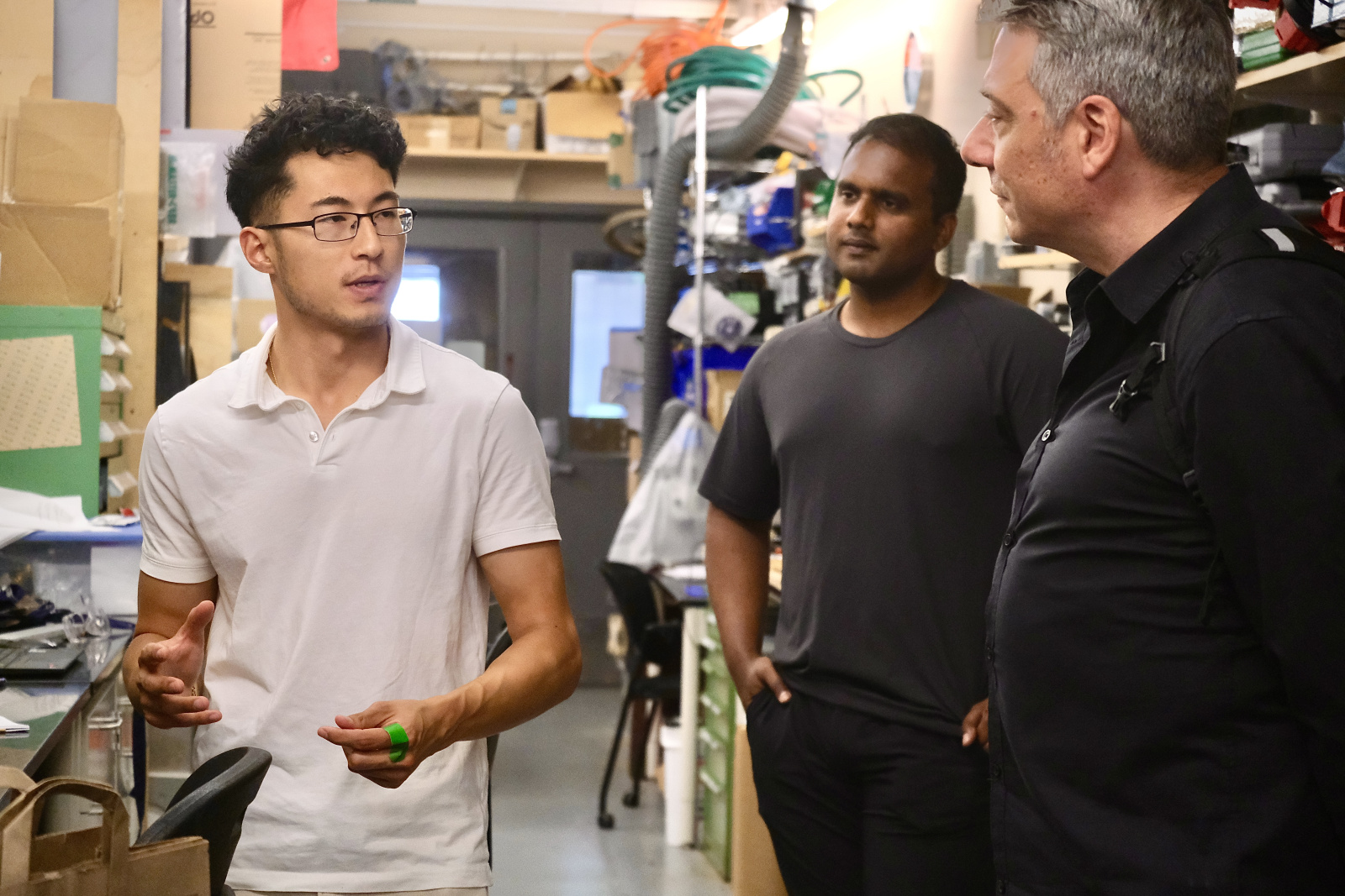 Jonathan in a white polo shirt speaks to two other men in a workshop filled with various tools and equipment.