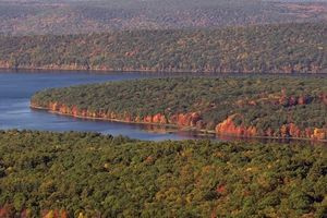 Aerial view of the Quabbin Reservoir with trees on either side, some with green leaves and some with red leaves. The water is a dark blue color.