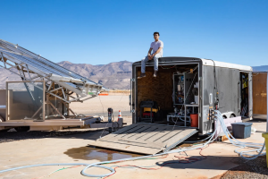 A photo of Jon Bessette sitting on top of a trailer surrounded by a solar powered desalination system. 