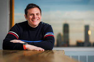 Andrew Babbin sitting at a table in front of a window displaying a city skyline at sunset. 