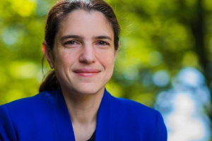 A woman wearing a blue blazer standing in front of a green background. 