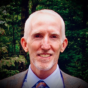 White man with beard and white hair, smiling with a suit jacket, shirt and tie