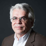 Headshot of Michael Triantafyllou wearing a white shirt with a brown jacket and glasses